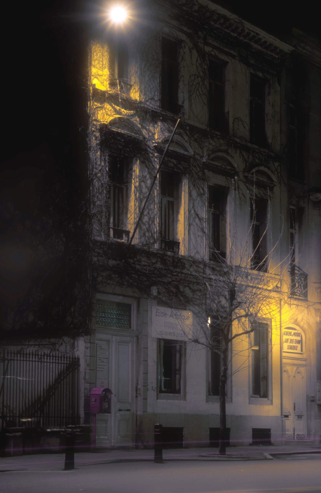 Façade d’un bâtiment ancien la nuit, une enseigne allumée et un réverbère au-dessus d’une rue déserte