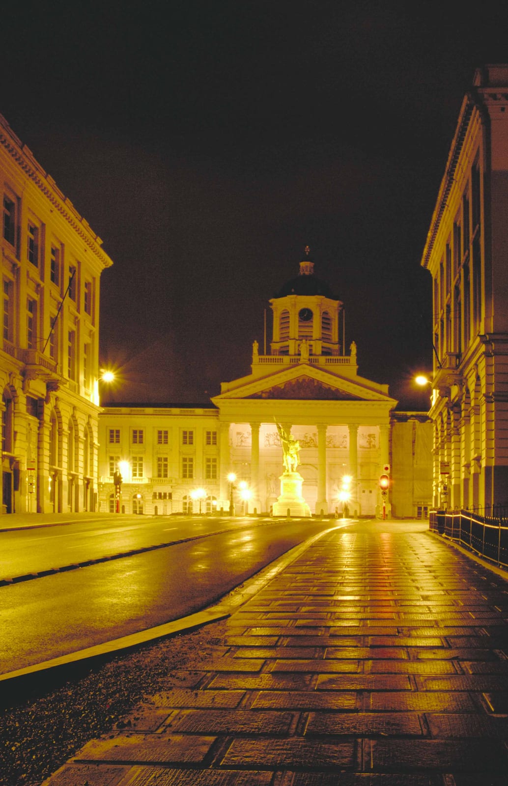 Une rue pavée montant vers un édifice à colonnes brillamment éclairé
