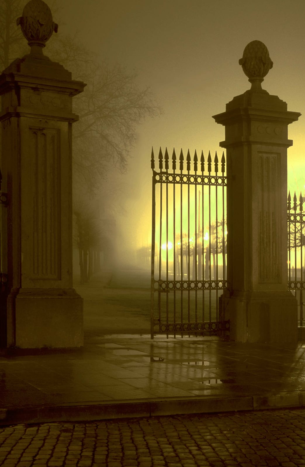 Les piliers d’une grille de parc dans la brume, une lueur dorée au-delà