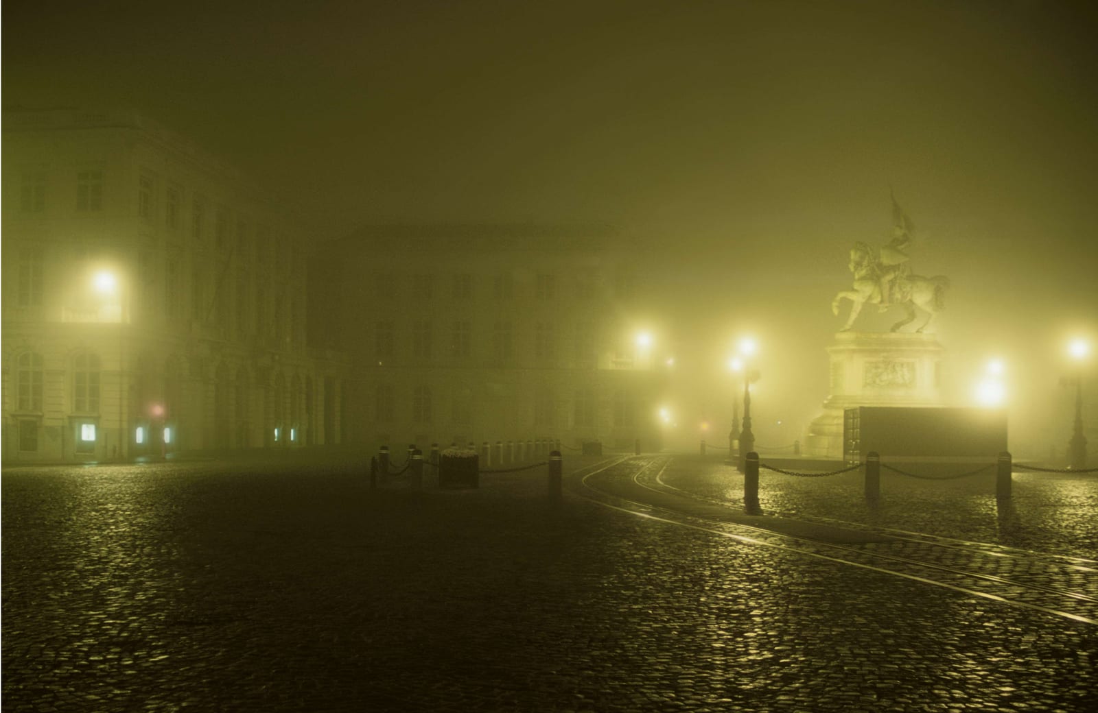 La place Royale sous un brouillard épais, pavés luisants et réverbères en enfilade