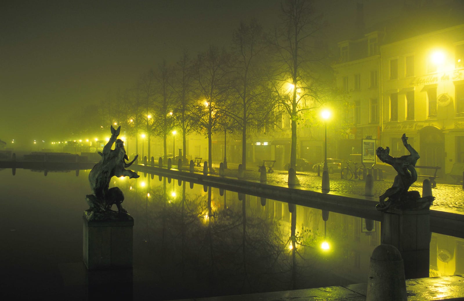 Un long bassin bordé de réverbères et de sculptures, leurs reflets s’étirant dans l’eau