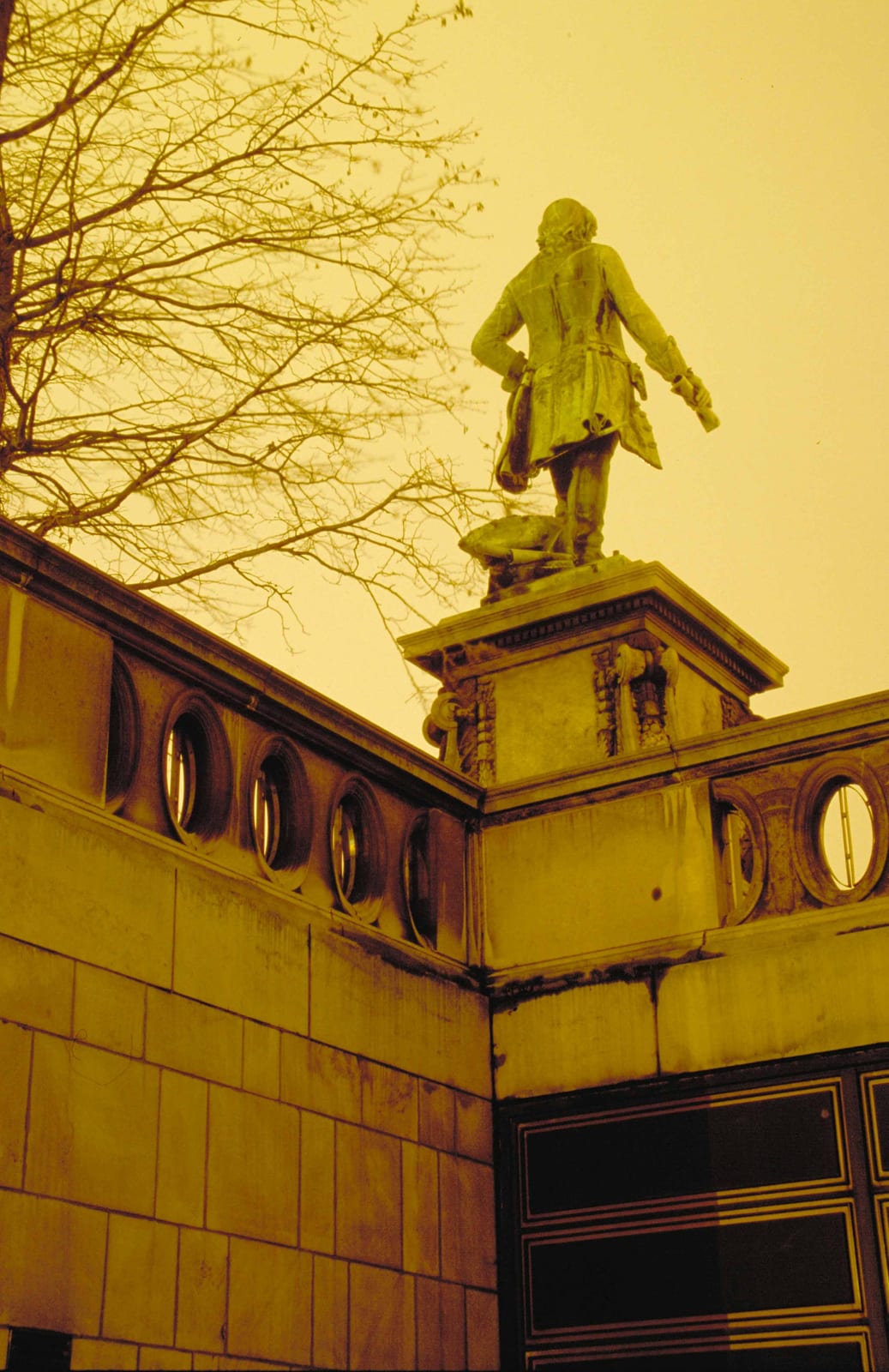 Une statue sur son socle vue en contre-plongée, contre un ciel de brume jaune