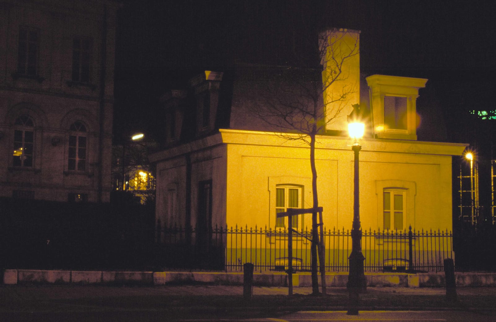 Un pavillon jaune vif derrière une grille, cerné par la nuit